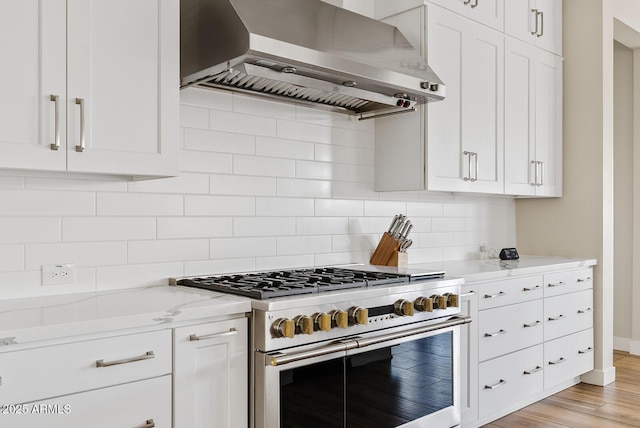 kitchen featuring decorative backsplash, white cabinets, wall chimney range hood, and range with two ovens