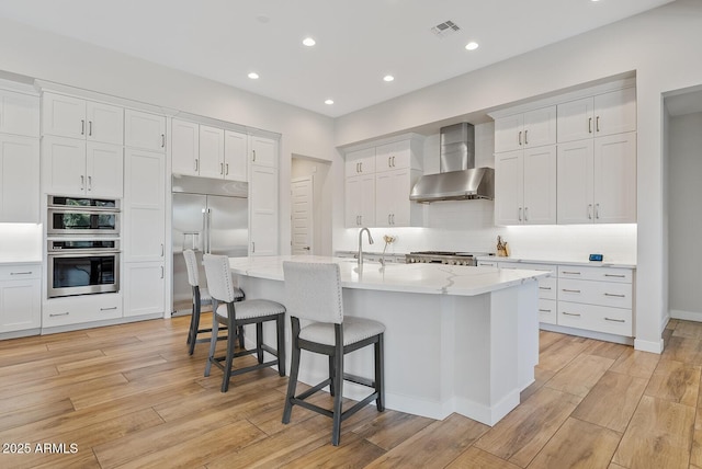kitchen with wall chimney range hood, decorative backsplash, stainless steel appliances, and white cabinets