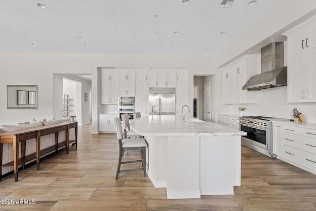 kitchen featuring decorative backsplash, light wood-style floors, wall chimney range hood, white cabinetry, and premium appliances