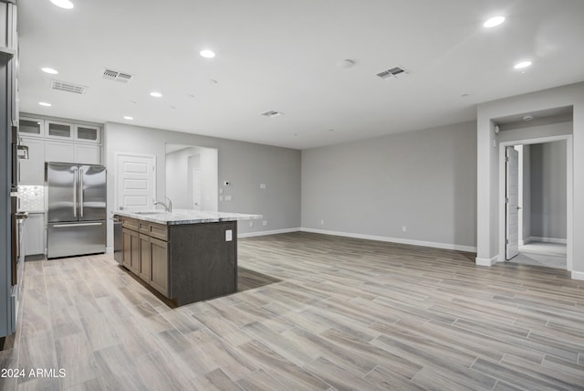 kitchen with light stone counters, stainless steel appliances, a kitchen island with sink, light hardwood / wood-style flooring, and white cabinets