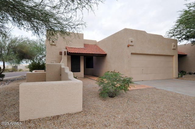 adobe home featuring a garage, concrete driveway, a tiled roof, and stucco siding