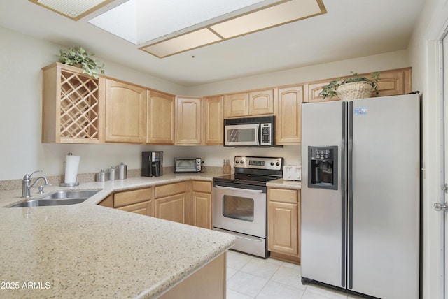 kitchen with a skylight, light tile patterned floors, appliances with stainless steel finishes, light brown cabinets, and a sink