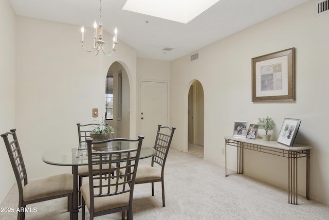 dining space with light colored carpet, arched walkways, a chandelier, and visible vents