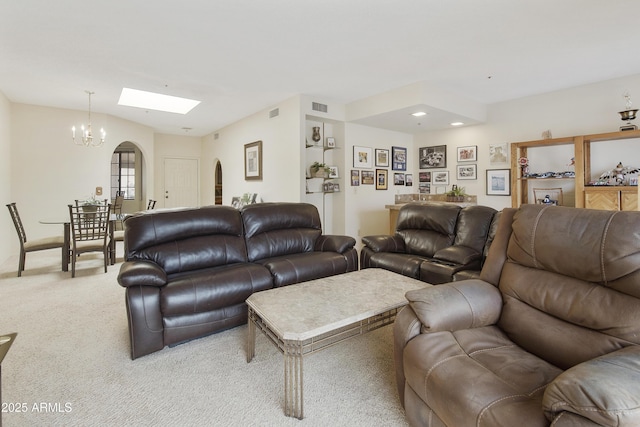 living room featuring light carpet, vaulted ceiling with skylight, visible vents, arched walkways, and an inviting chandelier