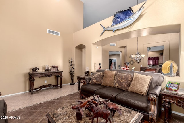 tiled living area featuring a chandelier, arched walkways, visible vents, and baseboards