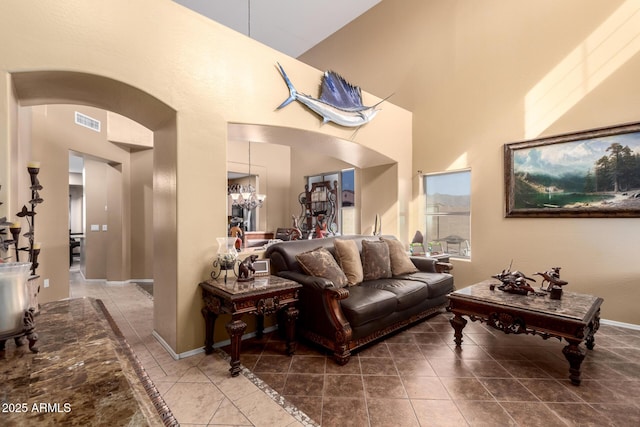 tiled living room featuring arched walkways, visible vents, an inviting chandelier, high vaulted ceiling, and baseboards