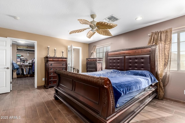 bedroom with a walk in closet, visible vents, a ceiling fan, wood tiled floor, and baseboards