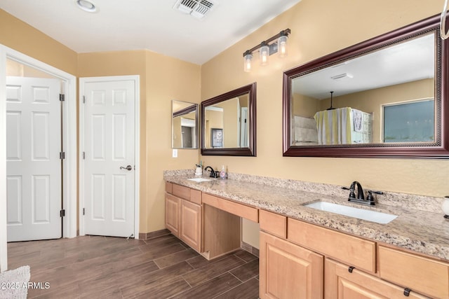 bathroom featuring double vanity, wood finish floors, a sink, and visible vents