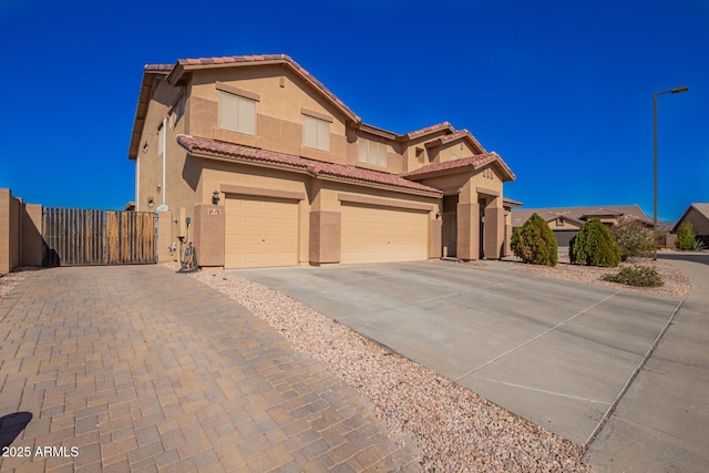 view of front of home with an attached garage, a tile roof, concrete driveway, a gate, and stucco siding