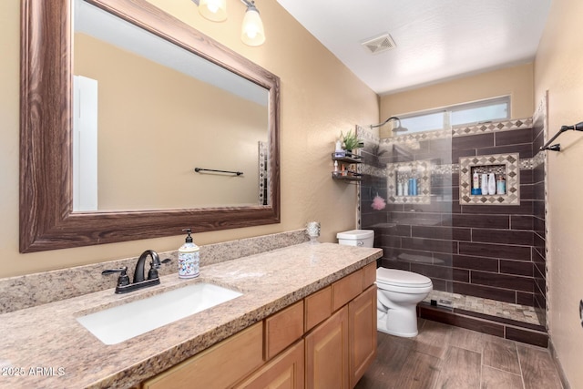 bathroom featuring visible vents, toilet, wood tiled floor, a tile shower, and vanity