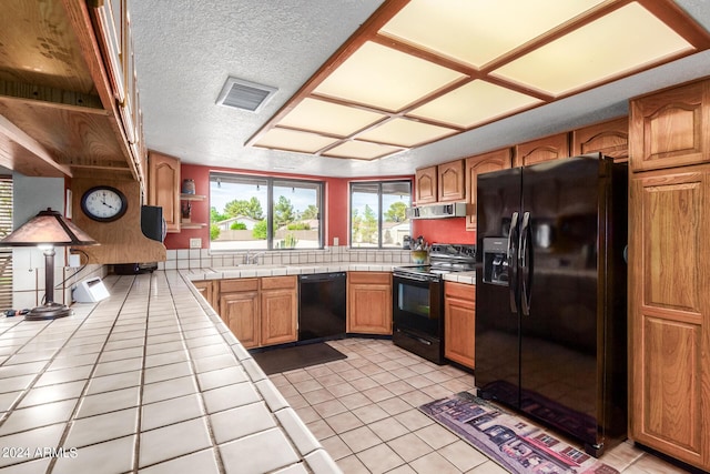 kitchen with black appliances, exhaust hood, sink, tile countertops, and light tile patterned flooring