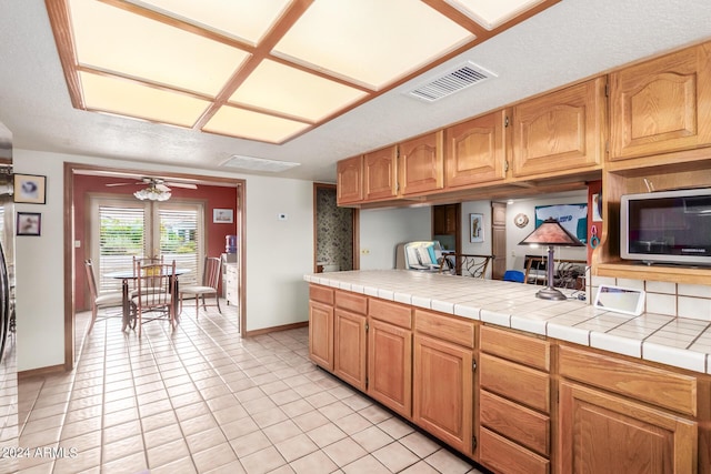 kitchen with light tile patterned floors, ceiling fan, and tile counters