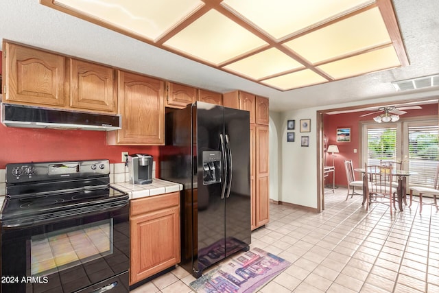 kitchen with light tile patterned flooring, black appliances, ceiling fan, and tile counters