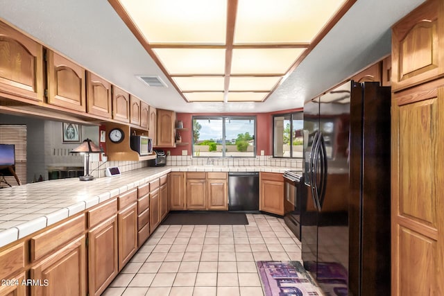 kitchen featuring sink, light tile patterned floors, black appliances, and tile countertops