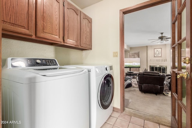 clothes washing area with ceiling fan, light tile patterned floors, a fireplace, cabinets, and washer and clothes dryer