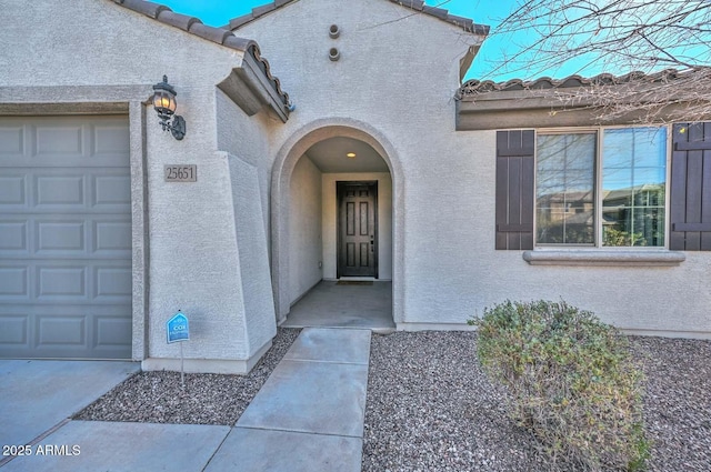 property entrance featuring a tiled roof, an attached garage, and stucco siding