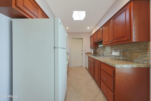 kitchen featuring light tile patterned floors, white appliances, a sink, backsplash, and brown cabinetry