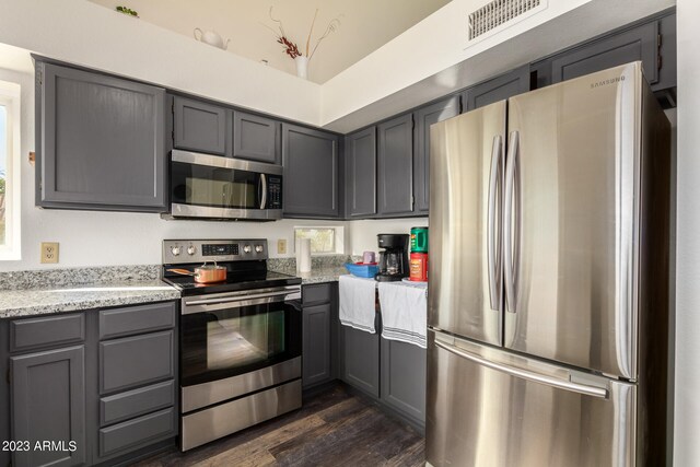 kitchen featuring gray cabinets, light stone counters, appliances with stainless steel finishes, and dark hardwood / wood-style flooring