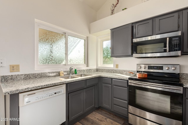 kitchen with appliances with stainless steel finishes, light stone counters, sink, gray cabinets, and dark hardwood / wood-style floors