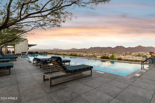 pool at dusk featuring a patio area and a water and mountain view