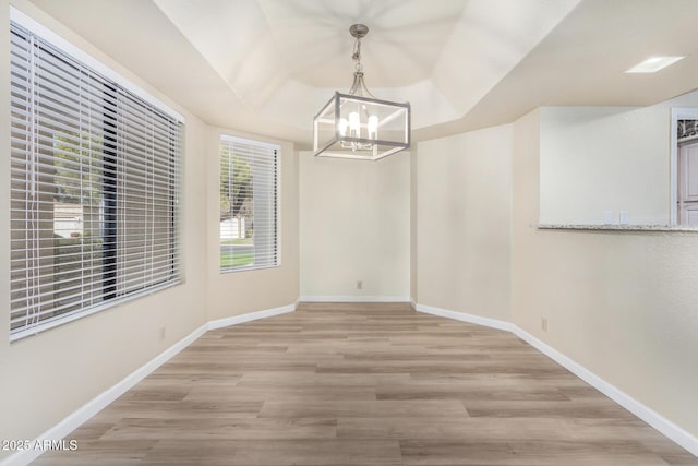 unfurnished dining area with a notable chandelier, a raised ceiling, and light wood-type flooring