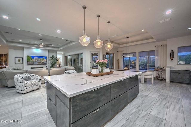 kitchen featuring ceiling fan, light stone counters, a spacious island, decorative light fixtures, and a tray ceiling