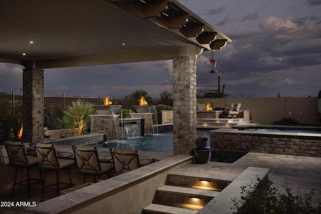 patio terrace at dusk featuring pool water feature, a fenced in pool, and exterior kitchen