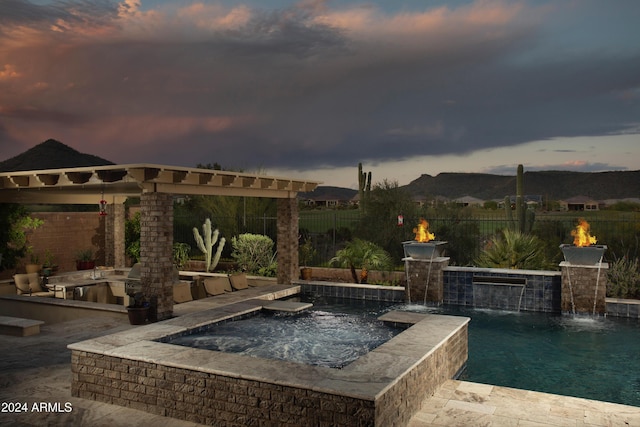 pool at dusk with pool water feature and an in ground hot tub