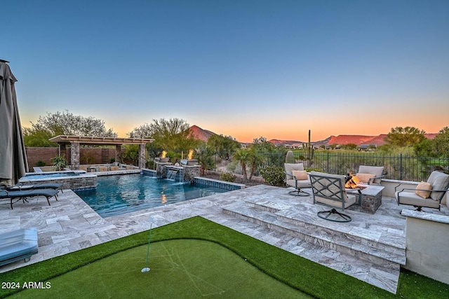 pool at dusk with a mountain view, pool water feature, an in ground hot tub, an outdoor living space with a fire pit, and a patio area