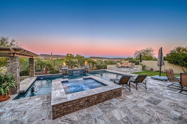 pool at dusk with pool water feature, a patio area, and an in ground hot tub