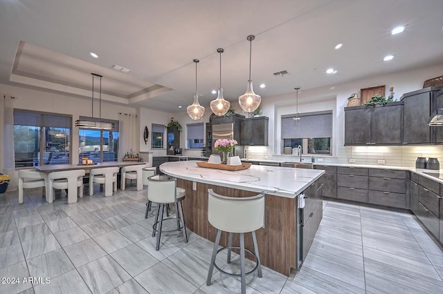 kitchen featuring pendant lighting, tasteful backsplash, a raised ceiling, and a spacious island