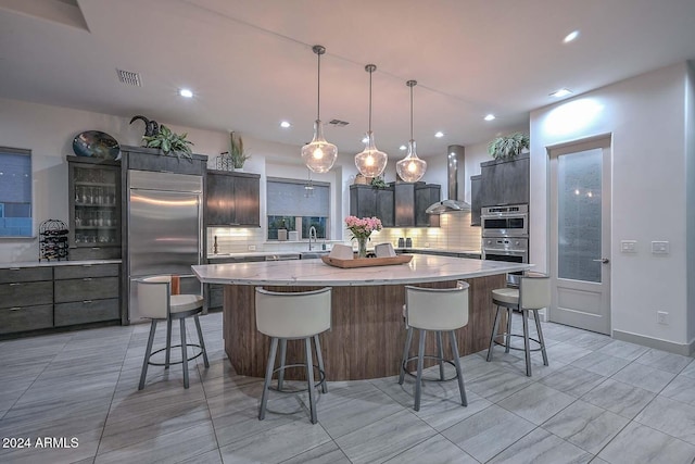 kitchen featuring a large island, sink, wall chimney range hood, backsplash, and appliances with stainless steel finishes