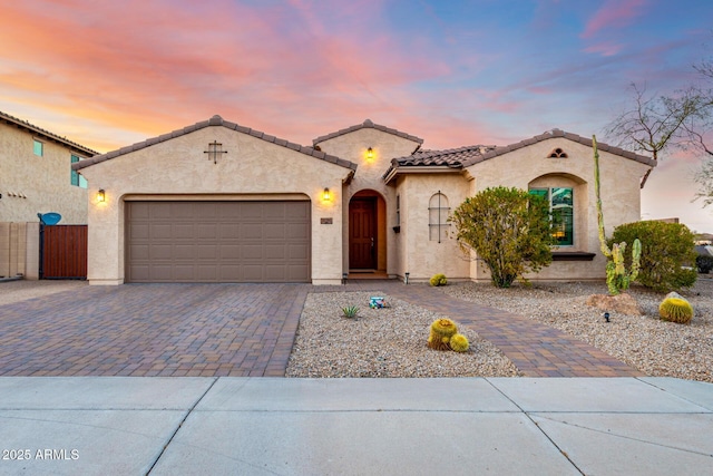 mediterranean / spanish home featuring stucco siding, decorative driveway, fence, a garage, and a tiled roof