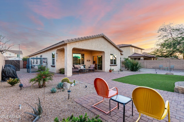 back of property at dusk featuring a patio, a yard, a fenced backyard, stucco siding, and outdoor lounge area