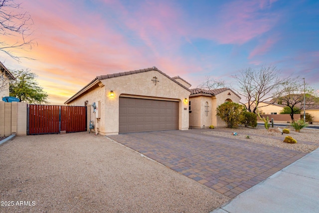 mediterranean / spanish house with stucco siding, a gate, decorative driveway, an attached garage, and a tiled roof