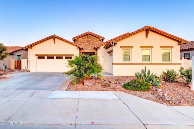 mediterranean / spanish home featuring stucco siding, concrete driveway, a garage, stone siding, and a tile roof