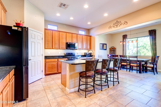 kitchen featuring visible vents, a kitchen island with sink, a sink, appliances with stainless steel finishes, and a breakfast bar area