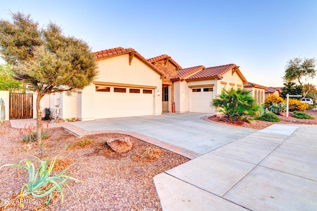 mediterranean / spanish-style house with stucco siding, a tile roof, fence, concrete driveway, and an attached garage