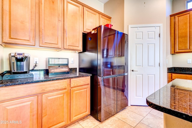 kitchen featuring dark stone counters, light tile patterned flooring, and freestanding refrigerator