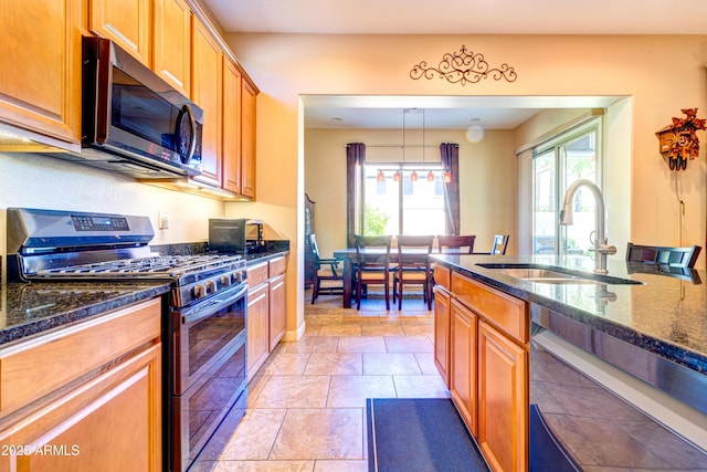 kitchen featuring pendant lighting, a sink, dark stone countertops, stainless steel appliances, and brown cabinetry