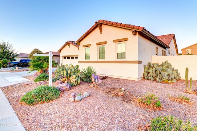 mediterranean / spanish house featuring stucco siding, fence, concrete driveway, an attached garage, and a tiled roof