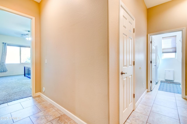 corridor with light tile patterned flooring, light colored carpet, and baseboards