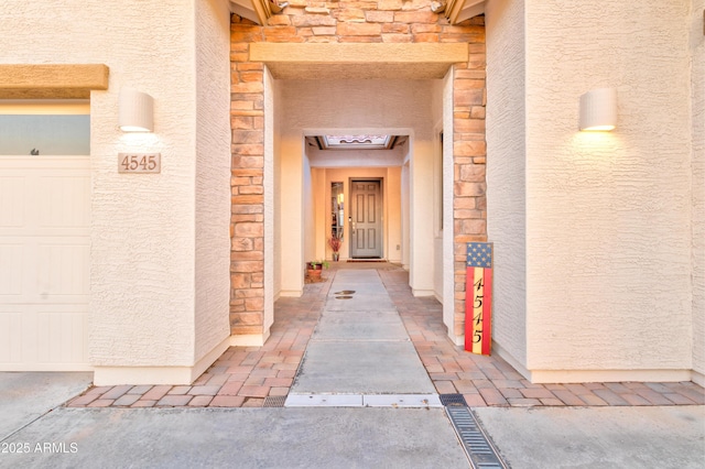 view of exterior entry featuring stucco siding, stone siding, and an attached garage