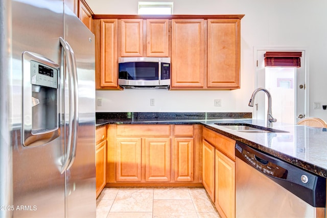 kitchen featuring a sink, appliances with stainless steel finishes, light tile patterned flooring, and dark stone countertops