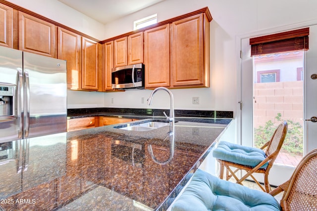 kitchen featuring dark stone countertops, a healthy amount of sunlight, appliances with stainless steel finishes, and a sink