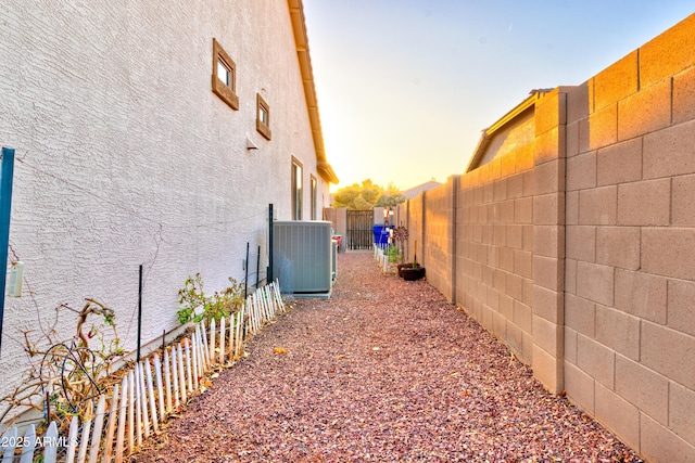 view of side of home featuring central AC unit, a fenced backyard, and stucco siding