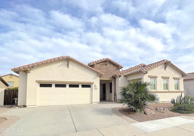 mediterranean / spanish-style house with an attached garage, a tiled roof, stucco siding, stone siding, and driveway