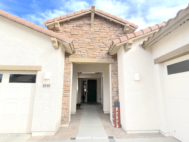view of exterior entry with a tiled roof, stucco siding, and stone siding