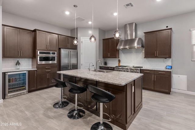 kitchen featuring wine cooler, wall chimney exhaust hood, sink, light stone counters, and appliances with stainless steel finishes