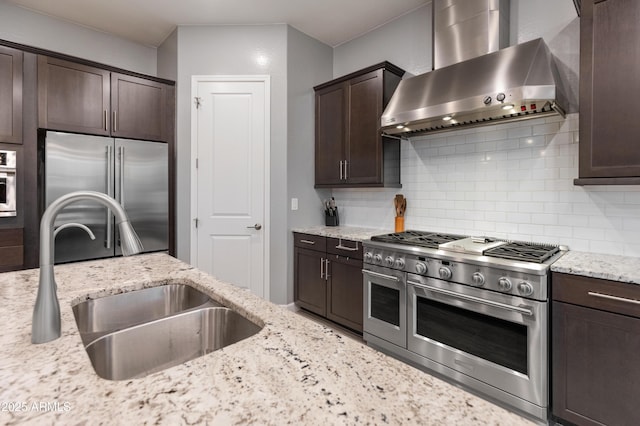 kitchen featuring high end appliances, sink, light stone countertops, and wall chimney exhaust hood